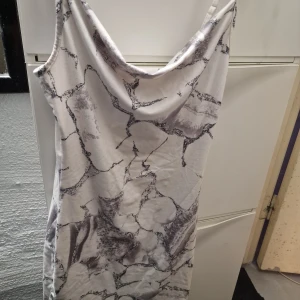 Mönstrad klänning - Snygg klänning med ett unikt mönster i svart och grått på vit bakgrund. Klänningen har en draperad halslinje och är ärmlös, vilket ger en elegant look. Perfekt för en stilfull kväll.