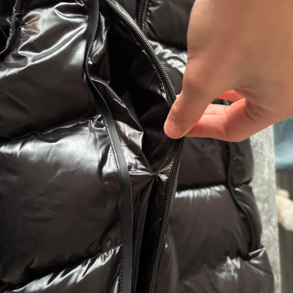 Snygg svart dunväst från Moncler med dragkedja och huva. Västen har en glansig finish och Moncler-logga på ryggen. Perfekt för kyligare dagar. Köpt för 1350 knappast använd . Takit.