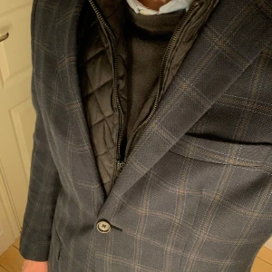 Mörkblå rutig kavaj från Riley - Riktigt snygg mörkblå kavaj med bruna inslag från Riley med rutmönster i riktigt bra skick. Storlek 48. Material är främst ull och linne. Priset är inte hugget i sten