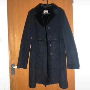 Svart kappa från Joy - Elegant svart kappa från Joy med knappar framtill och mjukt foder. Perfekt för kyliga dagar med sin stilrena design och bekväma passform.