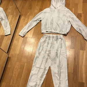 Gråmelerad hoodie och byxor från Gina  - Säljer ett set med en gråmelerad hoodie och matchande byxor från Gina Tricot. Hoodien har en bekväm passform med långa ärmar och en justerbar huva. Byxorna har elastisk midja för extra komfort. Perfekt för en avslappnad stil.🤍