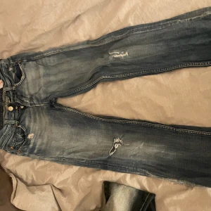 Blå jeans med slitningar - Säljer ett par blå jeans med coola slitningar och en klassisk femficksdesign. Jeansen har en knappgylf och är i en snygg tvättad look. de är i storlek 28/32 straight leg och low/midwaist. alldrig använt, bara testat