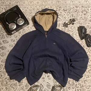 Mörkblå hoodie från Nike - Säljer en mörkblå hoodie från Nike med dragkedja och huva. Den har en liten Nike-logga broderad på bröstet och en beige insida i huvan. Perfekt för en avslappnad stil. Storlek M, skulle säga att den är lite kortare än vanligt, men sitter riktigt snyggt om man har snyggt bälte till jeansen ‼️