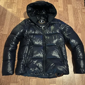 Save the duck jacka - Snygg svart pufferjacka från Save the Duck. Jackan har en glansig finish och är varm. Såklart är jackan äkta. Skriv om ni har några frågor. 