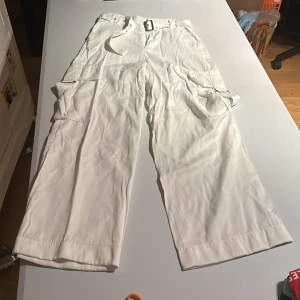 Vita cargopants med bälte f ån Zara stl S - Snygga vita cargopants med flera fickor och ett justerbart bälte. Byxorna har en loose passform och är perfekta för en avslappnad stil. De har praktiska detaljer som knappar och dragkedja. Knapp saknas i linningen men kan skickas med lös. 