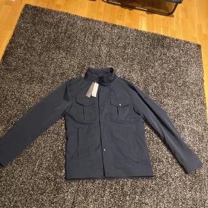 Field jacket bailey poly jacket  - En snygg och stillren marinblå field jacket till hösten fårn J.lindeberg. Köpte den i slutet på sommaren från J.lindebergs hemsida för fullpris. Storlek S, kan passa M. Helt oanvänd och lapparna sitter kvar. 
