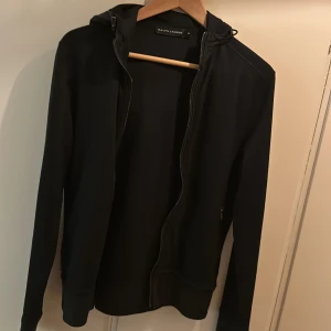 Svart kofta från Ralph Lauren - Snygg svart kofta/tröja från Ralph Lauren med dragkedja och huva. Perfekt för en stilren och avslappnad look. Tillverkad i mjukt material för extra komfort.
