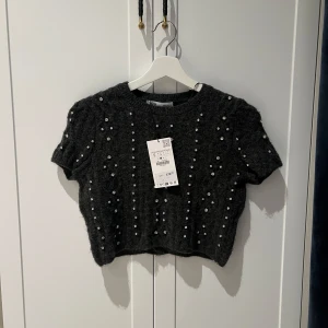 Mörkgrå stickad topp från Zara - Mörkgrå stickad topp från Zara med korta ärmar och små kristaller✨ Toppen är i storlek S och lite kortare i modellen, passar bra på mig som är XS/32. Ser bredare ut över axlarna än vad den är pga galge! Ny med prislapp kvar🎀