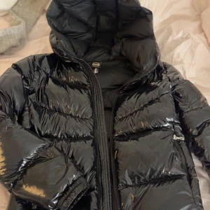 Svart glansig dunjacka från Colmar - Snygg svart glansig dunjacka från Colmar med huva och dragkedja. Perfekt för kyliga dagar med sin pufferdesign som håller värmen. Inga defekter eller liknande💗storlek 14år men passar bra på mig som vanligtvis bär xs 