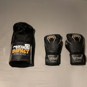 Venum Impact Boxningshandskar - Säljer ett par boxningshandskar i mörk camo-design. De är svarta med ett mönster och har Venumloggan på framsidan. Jag gick i thaiboxning i en vecka och sen tappade jag intresset för det. Som nya och kommer i original förpackningen. köpte dem för 750