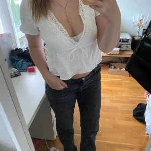 Vit blus med spetsdetaljer - Säljer en superfin vit blus med spetsdetaljer runt den v-ringade halsen. Blusen har korta ärmar och en söt knytning framtill. Perfekt för sommardagar eller en avslappnad fest. Den är i bra skick och passar till både jeans och kjol!