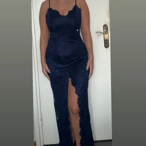 Mörkblå spetsklänning med slits - Säljer en elegant mörkblå långklänning i spets. Klänningen har smala axelband och en vacker slits framtill som ger en sofistikerad look. Perfekt för festliga tillfällen!