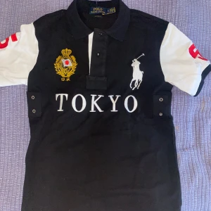 Ralph lauren piké - "Säljer en pikétröja från Ralph Lauren i utmärkt skick. Den har snygga detaljer med texten 'Tokyo' broderat på framsidan, och färgpaletten består av rött, vitt och svart. En stilren och unik tröja. Skicka gärna ett meddelande för mer info eller mått!
