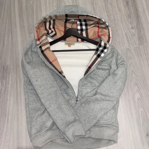 Grå hoodie med mönstrad huva - Säljer en snygg grå hoodie från Burberry med en klassisk mönstrad huva i beige, svart och. Superbekväm och stilren! Använd 4-5 gånger. Skriv gärna eran prisförslag! KAN SÄNKAS VID SNABB affär