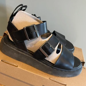 Svarta sandaler med spännen - Svarta sandaler fr Dr. Martens i modell Gryphon, robust sula och justerbara spännen för perfekt passform. Perfekta för sommarens äventyr men även vår och höst till kjol och ett par snygga strumpor. Finns att köpa för 1400 på nätet. Knappt använda!