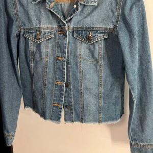 Jeansjacka från Nelly - Snygg jeansjacka från Nelly i perfekt skick. Jackan har en klassisk design med en modern twist som passar både till vardags och fest. Den har en bekväm passform och är lätt att matcha med olika outfits. Använd endast ett fåtal gånger. 