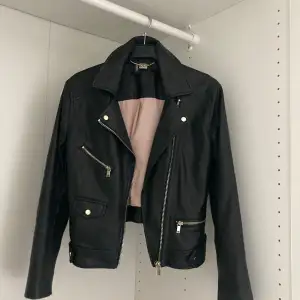 Säljer en snygg svart skinnjacka från H&M. Jackan har en cool bikerstil med dragkedjor och knappar i silverfärg. Den är fodrad med ett ljust tyg på insidan och har en klassisk krage. Perfekt för höst och vår! Slitage på sista bilden på nacken.