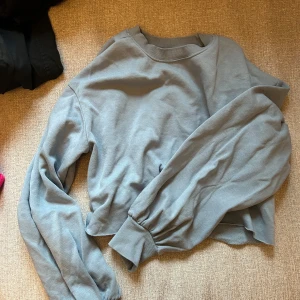 Blå croppad sweatshirt - Säljer en stilren grå croppad sweatshirt med långa ärmar och ribbade muddar. Perfekt för en avslappnad look. Passar bra till jeans eller leggings.