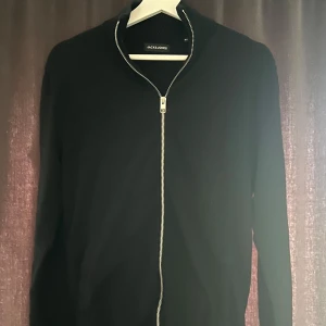 Svart kofta från Jack & Jones - Säljer en stilren svart kofta från Jack & Jones i storlek XS. Koftan har en praktisk dragkedja framtill och är perfekt för lager-på-lager-stil. Passar både till vardags och mer uppklädda tillfällen. Hör gärna av er vid ytterligare frågor mvh✌️