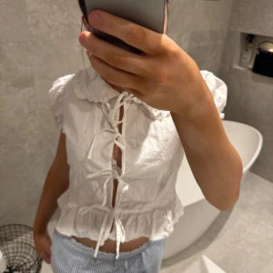 Vit blus med knytning - Charmig vit blus med knytning framtill och volangdetaljer. Den har korta ärmar och en söt krage. Perfekt för en somrig look!