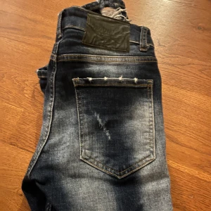 Mörkblå jeans från Dsquared2 - Snygga mörkblå jeans från Dsquared2 med slitna detaljer och en cool tvätt. Byxorna är i nyskick och nypris är 2500. Hör av er över minsta lilla!