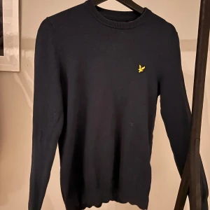 Mörkblå tröja från Lyle & Scott - Snygg mörkblå tröja från Lyle & Scott med deras ikoniska gula logga på bröstet. Tröjan har en klassisk rund hals och långa ärmar, perfekt för en stilren look.