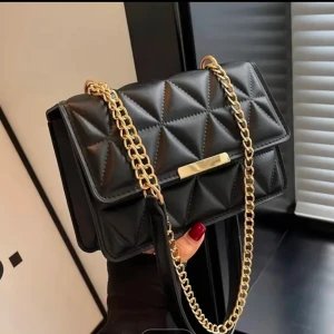 Svart quiltad axelväska med guldkedja - Snygg svart axelväska med quiltat mönster och elegant guldkedja. Väskan har en stilren design med en praktisk storlek för att bära dina nödvändigheter. Perfekt för att ge din outfit en lyxig touch.