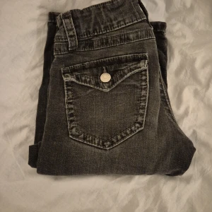 Svarta jeans från Gina Tricot - Snygga svarta lågmidjade bootcut jeans från Gina Tricot med klassisk femficksdesign och knappgylf. Perfekta för en stilren look. Passar bra till både vardag och mer uppklädda tillfällen.