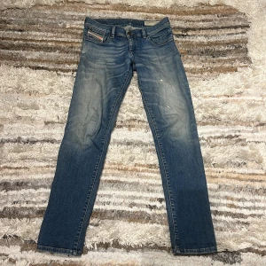 Blå jeans från Diesel - Snygga blå jeans från Diesel med en klassisk femficksdesign och lätt slitna detaljer för en cool look. De har en rak passform och är perfekta för en avslappnad stil. Märkeslogga på den lilla fickan ger en extra touch. Nyskick.