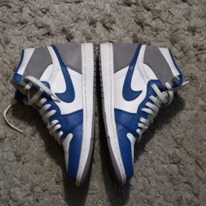 Nike Jordan 1 High "True Blue" retro og - Snygga Nike sneakers i blått, vitt och grått som är i nyskick. Perfekta för en stilren look. Kommer med originalkartong och extra par blåa skosnör.               (PRIS KAN FÖRHANDLAS)