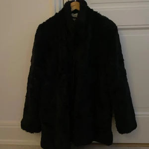 Svart pälsjacka från Tiger of Sweden - Säljer en elegant svart fusk pälsjacka från Tiger of Sweden i storlek medium. Jackan har en lyxig känsla med långärmad design och en stilren look. Perfekt för att hålla sig varm och snygg under kyliga dagar. Rockhängaren har gått av vid andra sidan men ska funka att bara sy på den. Man kan även hänga upp jackan med märkeslapparna i kragen istället. 