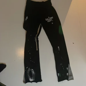 Svarta byxor från Gallery Dept. - Unika svarta byxor från Gallery Dept. med vita och gröna detaljer. Byxorna har en avslappnad passform och är dekorerade med ett konstnärligt mönster. De har en elastisk midja med snörning för justerbar passform. Skick 10/10