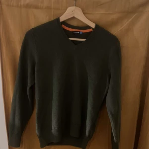 Grön tröja från J.Lindeberg - Säljer en stilren grön tröja från J.Lindeberg. Tröjan har en v-ringad hals och långa ärmar, perfekt för kyligare dagar. Den är tillverkad i ett mjukt material som ger en bekväm passform. Passar bra till både jeans och chinos.