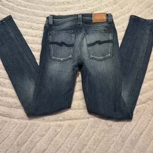 Blå jeans från Nudie Jeans - Snygga blå jeans från Nudie Jeans med klassisk femficksdesign och en cool tvätt. De har en normal passform och är perfekta för en avslappnad stil. Märkeslogga på bakfickan ger en extra touch. Storlek W27 L32