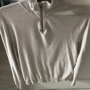 Beige tröja med dragkedja från Jack & Jones - Säljer en stilren beige tröja från Jack & Jones med dragkedja vid halsen. Tröjan har långa ärmar och en ribbad krage samt nederkant. Perfekt för en avslappnad look. Kan gå ner i pris vi snabb och smidig affär 