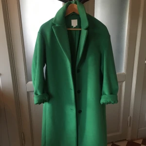 Grön kappa från hm storlek small - Snygg grön kappa med klassisk design och knappar framtill. Perfekt för att lysa upp din garderob med en färgklick. Den har långa ärmar och en stilren krage.