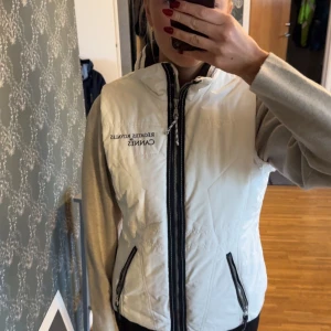 Vit fodrad väst från Marinepool - Säljer en stilren vit fodrad väst från Marinepool, del av Régates Royales de Cannes-kollektionen. Västen har dragkedja framtill och broderad text på bröstet pch ryggen. Sparsamt använd, mkt bra skick. 