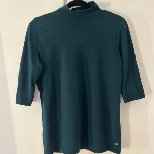 Mörkgrön polotröja - Säljer en stilren mörkgrön polotröja med trekvartsärm. Perfekt för en elegant och avslappnad look. Tröjan har en enkel design som gör den lätt att matcha med olika outfits.