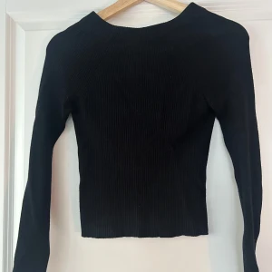 Svart ribbad tröja med knyt - Snygg svart ribbad tröja med lång ärm och knytning i ryggen. Perfekt för en stilren look.