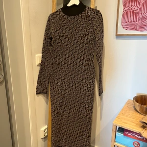 Mönstrad långklänning med hög krage - Snygg långklänning med geometriskt mönster i svart och beige. Klänningen har en hög ribbad krage och långa ärmar. Materialet känns mjukt och bekvämt. Klänningen är ifrån Chiquelle och är i strl S/M. Använd fåtal gånger men är som ny✨