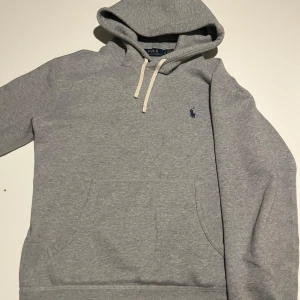 Grå hoodie från Polo Ralph Lauren - Säljer en stilren grå hoodie från Polo Ralph Lauren med klassisk känguruficka och justerbar huva med snören. Den har en liten broderad logga på bröstet. Perfekt för en avslappnad stil. Liten näst in till osynlig defekt på fickan men annars är tröjan i ny skick. Hör av dig vid minsta fundering Mvh Charlie
