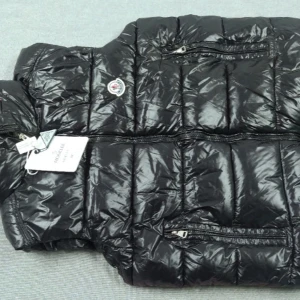 Svart dunväst från Moncler - Snygg svart dunväst från Moncler med glansig yta och dragkedjor på fickorna. Perfekt för kyligare dagar och ger en stilren look. Västen har en broderad logga på bröstet.