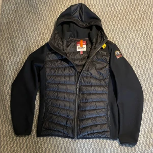 Svart jacka från Parajumpers - Säljer en svart jacka från Parajumpers. Lagad på 2 ställen, se bilder men i övrigt i mycket fint skick.             PRODUKTBESKRIVNING Tillverkad i polyamid och polyester. Armar tillverkade i mesh. Dunfyllning fram- och baktill. Två framfickor. Två innerfickor. En bröstficka med dragkedja. Ytterficka med dragkedja på baksidan. Emblem på vänster ärm. Dragskohuva. Lufthål vid respektive ärmhåla. Tvåvägsdragkedja. 