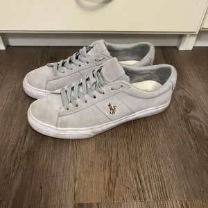 Grå sneakers från Polo Ralph Lauren - Snygga grå sneakers i mocka från Polo Ralph Lauren med klassisk snörning och den ikoniska loggan på sidan. Perfekta för en stilren look. Dem är smutsiga men i ett mycket bra skick, storlek 40 men passar även 41. Hör av er vid frågor.