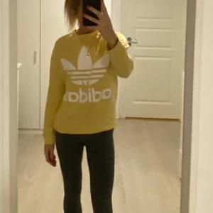Gul sweatshirt från Adidas - Säljer en ljusgul sweatshirt från Adidas med det klassiska trefoil-logotypen i vitt på framsidan. Tröjan har en rund hals och långa ärmar, perfekt för en avslappnad stil. Passar bra till både jeans och träningsbyxor.