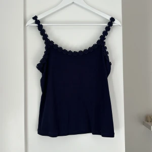 Mörkblå linnetopp från & Other Stories - Säljer en mörkblå linnetopp från & Other Stories med fina blommiga detaljer längs axelbanden. Perfekt för en stilren och somrig look. Toppen är ärmlös och har en mjuk och bekväm passform.