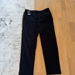 Mörkblå kostymbyxor från Massimo Dutti - Eleganta mörkblå kostymbyxor från Massimo Dutti med dragkedja och knappar. Perfekta för en stilren look. Byxorna har en klassisk passform och är tillverkade i ett bekvämt material.aldrig använda