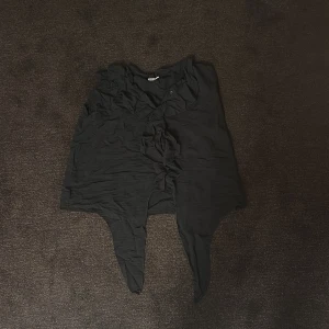 Svart asymmetrisk topp - Säljer en svart asymmetrisk topp med knytning framtill. Toppen har en unik design med oregelbundna kanter och är perfekt för en trendig look.