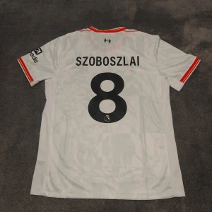 Liverpool FC | 24/25 | Szoboszlai | Size:L | Ny, oanvänd  - Liverpools tredjetröja för närvarande säsong 2024/25. Szoboszlai, nr 8 på ryggen. Storlek L. Helt ny & oanvänd. Stadium/fan edition. Tröjan är en nyproducerad reprint i utmärkt kvalitet.  Skickas 1-3 dagar efter mottagen betalning. Har du frågor/funderingar är det bara att höra av dig! :)