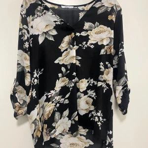 Svart blommig blus från Hailys - Snygg svart blus från Hailys med ett vackert blommigt mönster i beige och vita nyanser. Blusen har trekvartsärmar och en v-ringad halslinje. Perfekt för en stilren look.Skriv för fler bilder eller om ni har fler frågor 💓
